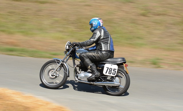Muž v čiernej koženej bunde a nohaviciach, s modrou prilbou na hlave ide na motorke.jpg